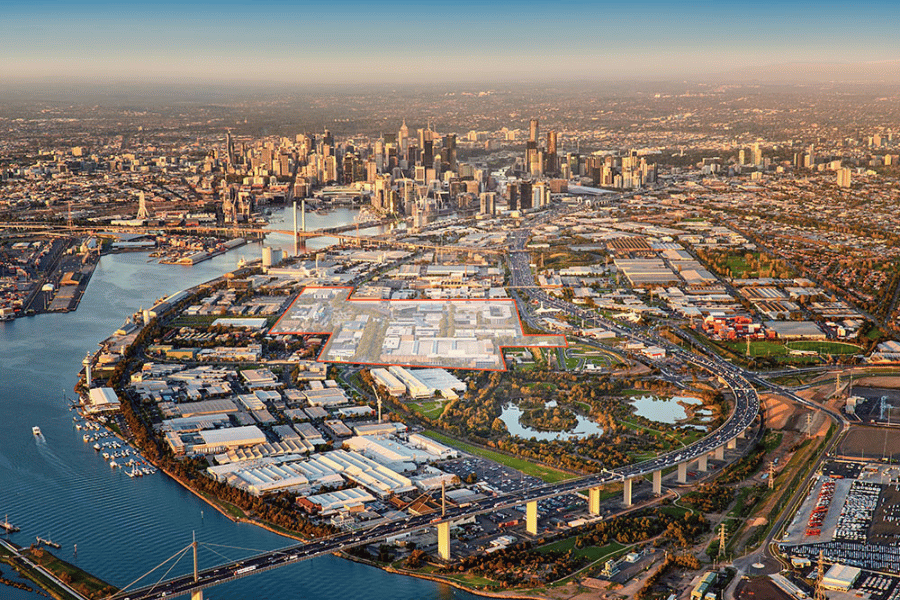 Aerial photograph showcasing an urban waterfront area with industrial buildings, green parkland, and a large river curving through the landscape. The city skyline with numerous skyscrapers appears in the background, highlighting the contrast between natural spaces and dense urban development.  