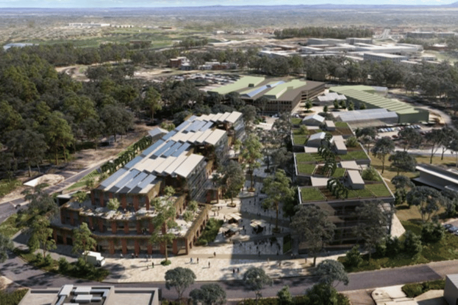 Aerial photograph of a modern eco-friendly urban development featuring multiple buildings with solar panels and green roofs surrounded by trees. The layout includes pedestrian pathways, open spaces, and a mix of residential and commercial structures emphasizing sustainability and integration with natural environment.